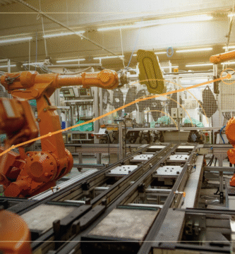 Composición editorial exclusiva de un brazo robótico industrial con trayectoria de movimientos ilustrativa en color ámbar, para explicar cómo entrenan los robots con inteligencia artificial. Foto original de Simon Kadula, Unsplash.